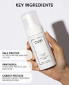 OUAI hair product held by a hand with key ingredients listed on a white background