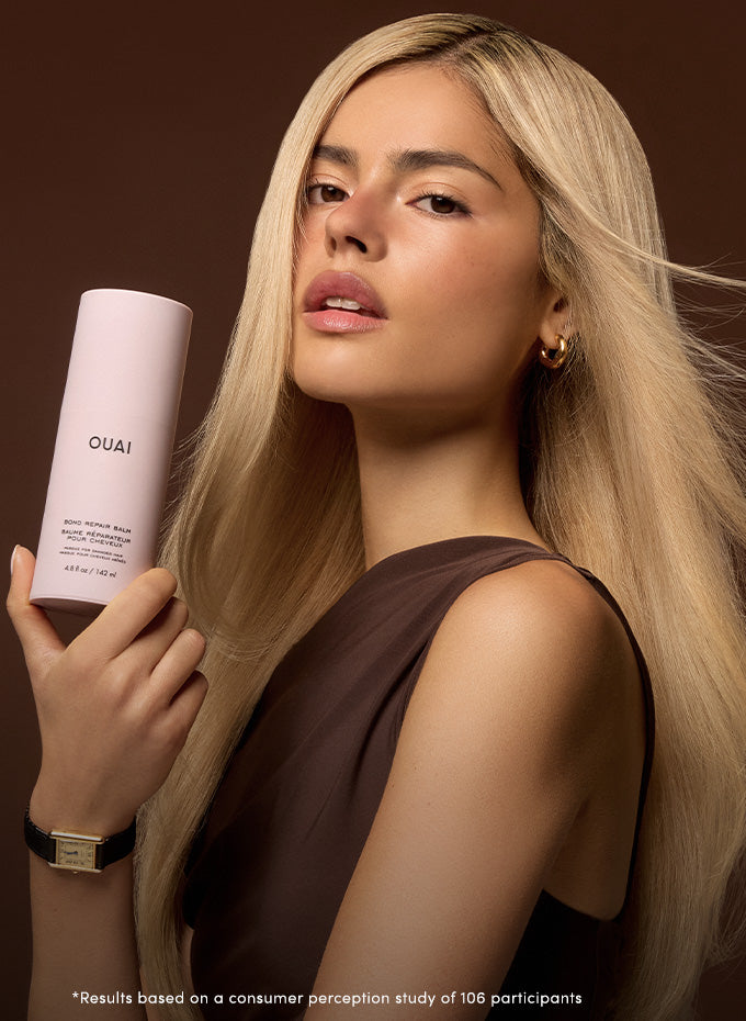 Woman holding a OUAI hair product against a brown background
