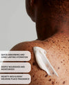 Close-up of a person's bare shoulder and upper back with a dollop of white body cream applied, plus three text callouts describing moisturizing and fragrance benefits.