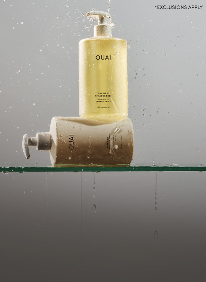 Two bottles of OUAI hair products on a glass shelf with a gray background.