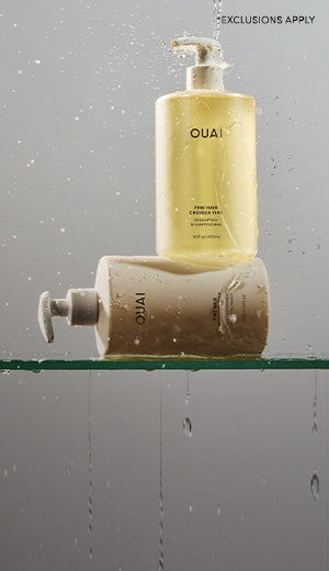 Two OUAI bottles on a glass shelf with water droplets on a gray background