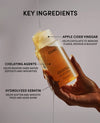 Hand holding a bottle of OUAI shampoo with labeled key ingredients on a neutral background