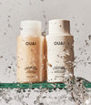 OUAI shampoo and conditioner bottles with water splashes on a gray background