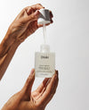 Hand holding OUAI scalp serum with dropper against a white background