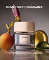 OUAI perfume bottle with fruit and flower elements on a reflective surface