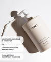OUAI Dean Street hand lotion in a matte off-white pump bottle, shown on a clean white background with a decorative smear of lotion and text callouts describing its moisturizing and citrus fragrance.