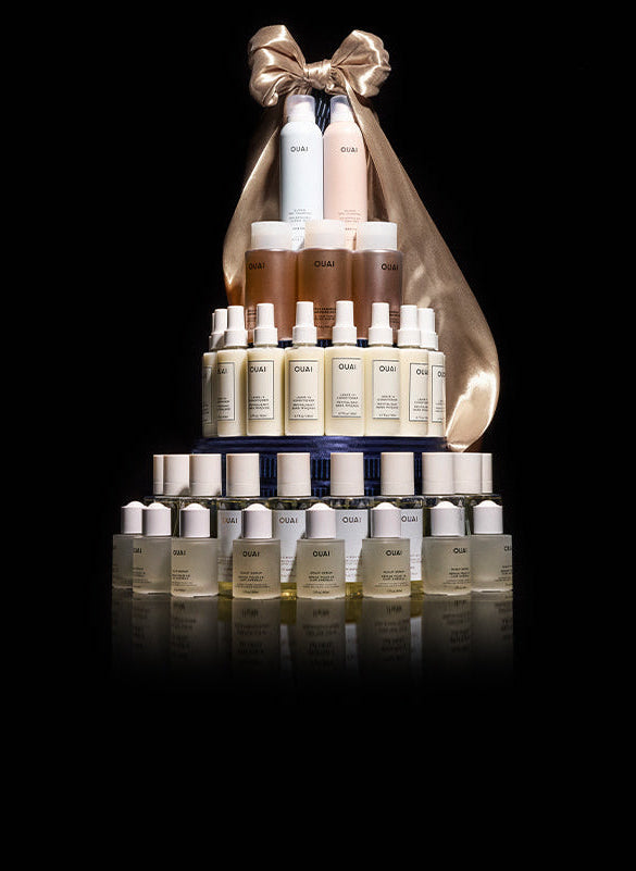 Tower of skincare bottles with a gold bow on a black background