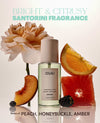 OUAI Santorini fragrance mist bottle centered on a light background, surrounded by peach, orange, grapefruit, and blackberry slices, with the text 'BRIGHT & CITRUSY SANTORINI FRAGRANCE' and 'Notes of: PEACH, HONEYSUCKLE, AMBER'.