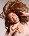 Woman with flowing red hair holding a bottle of shampoo against a neutral background