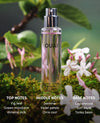 A clear cylindrical perfume bottle labeled OUAI stands on moss among green leaves and white flowers. Text at the bottom lists top, middle, and base notes for the fragrance.