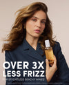 A woman with styled beachy waves holds a bottle of OUAI hair product against a plain beige background, with large text reading 'OVER 3X LESS FRIZZ FOR EFFORTLESS BEACHY WAVES'.