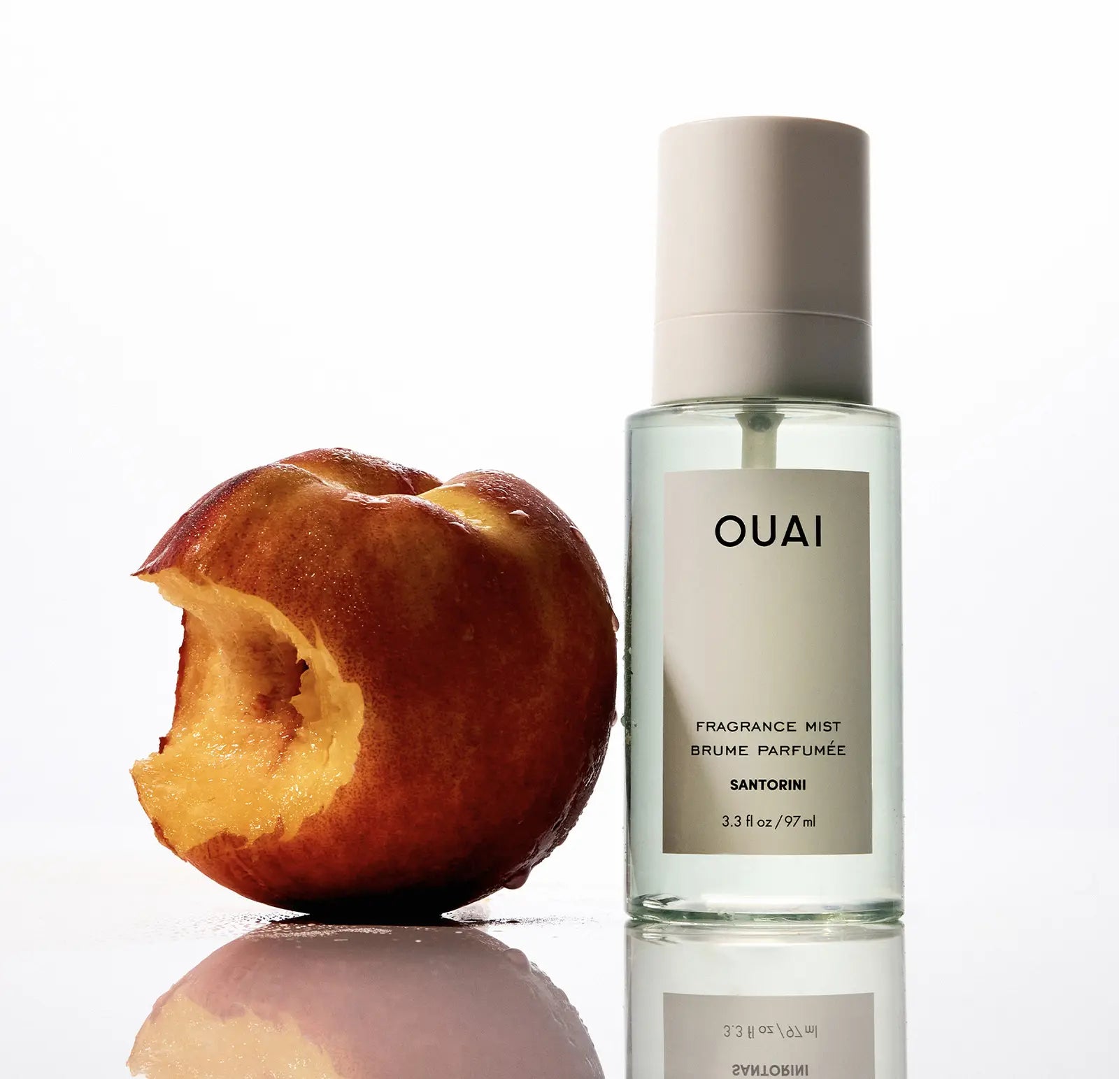 OUAI perfume bottle next to a bitten peach on a white background