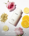 OUAI thick hair conditioner bottle in white, styled in a flat-lay with pink roses, lemon slices, and dried jasmine on a white background, with text overlay at the bottom.