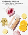 OUAI thick hair shampoo bottle on a white background with a pink rose, lemon slices, orange slices, and jasmine flowers, with text reading 'MERCER STREET FRAGRANCE Notes of: ITALIAN LEMON, TURKISH ROSE, IRIS & WHITE MUSK'.
