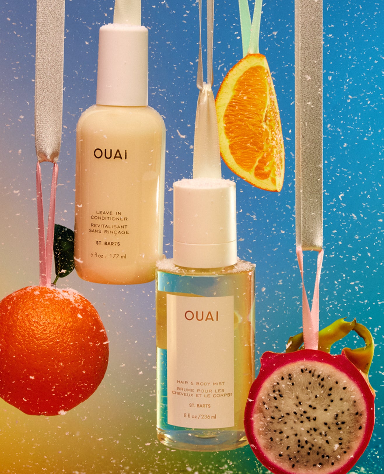 Three OUAI skincare bottles arranged against a bright blue gradient background with fruit slices and hanging straws. The bottles include a beige leave-in conditioner, a clear dropper bottle with a white cap, and a clear bottle with a white cap.