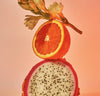 Dragon fruit cut in half with a halved orange on a pink background