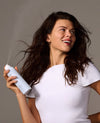 A woman with long hair holding a white spray bottle 