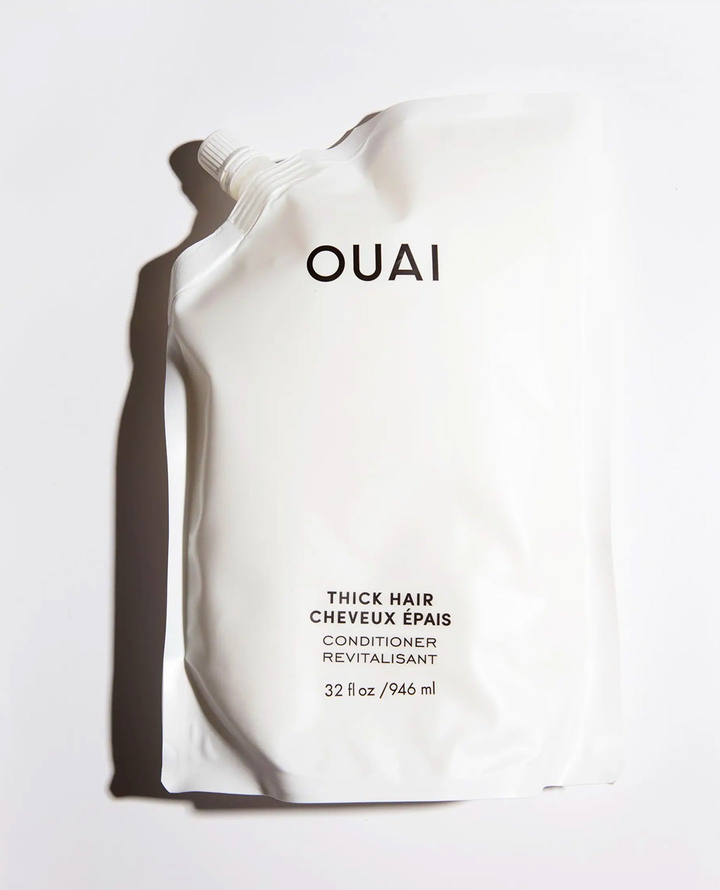 A white stand-up pouch of OUAI Thick Hair Conditioner with black text, photographed on a white background with a strong cast shadow.