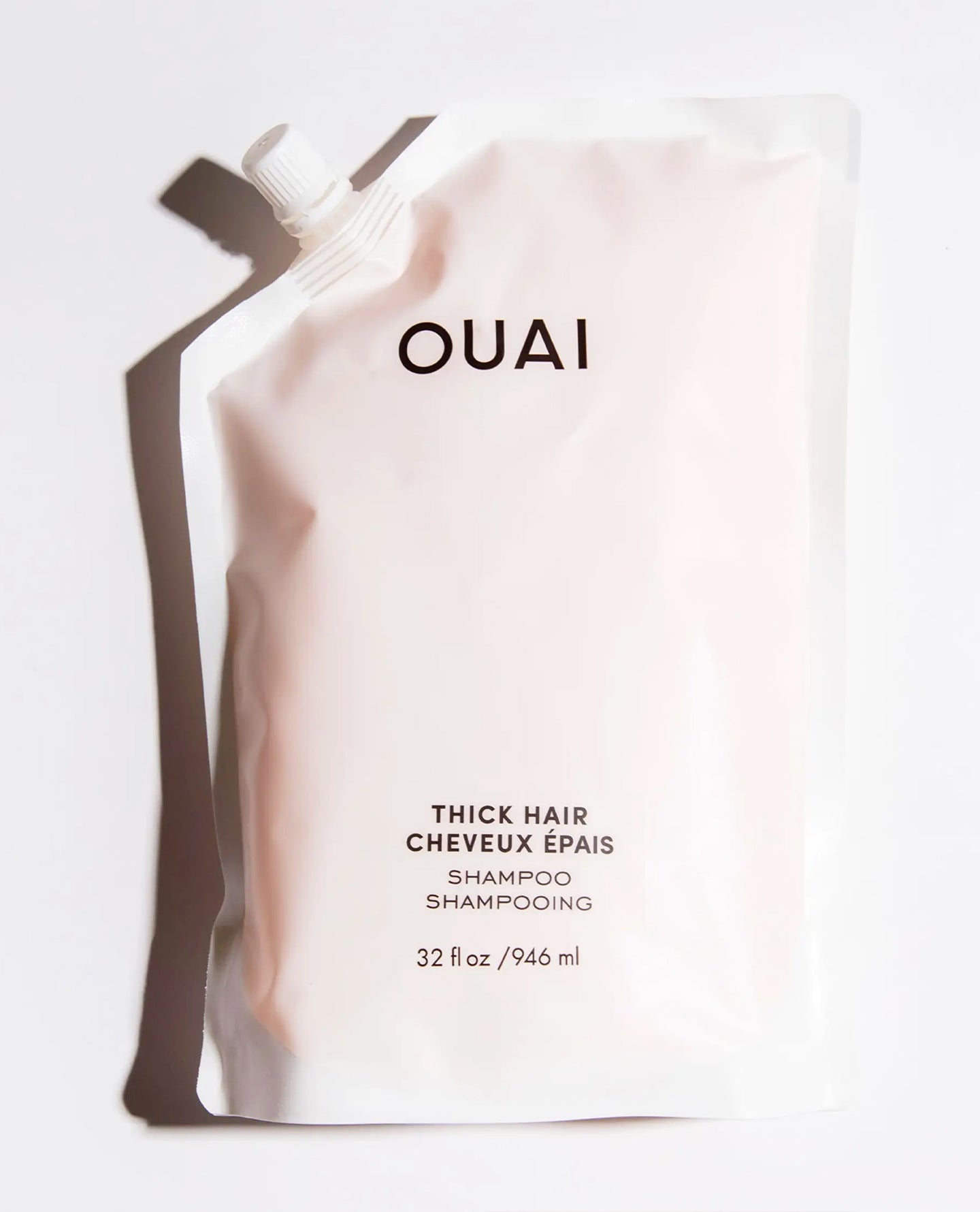 OUAI Thick Hair Shampoo refill pouch in a pale pink color, featuring black text and a white spout, photographed on a clean white background with a soft shadow.