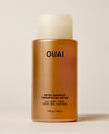 An amber OUAI shampoo bottle stands upright on a warm cream surface beneath a translucent cap. Text: “OUAI”, “DETOX SHAMPOO”, “SHAMPOOING DÉTOX”, “ALL HAIR TYPES”, “TOUS LES CHEVEUX”, “10 fl oz / 300 ml”.