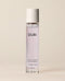 A slim clear OUAI Laurel Canyon eau de parfum bottle containing pale pink liquid stands upright against a warm, softly lit cream studio background.