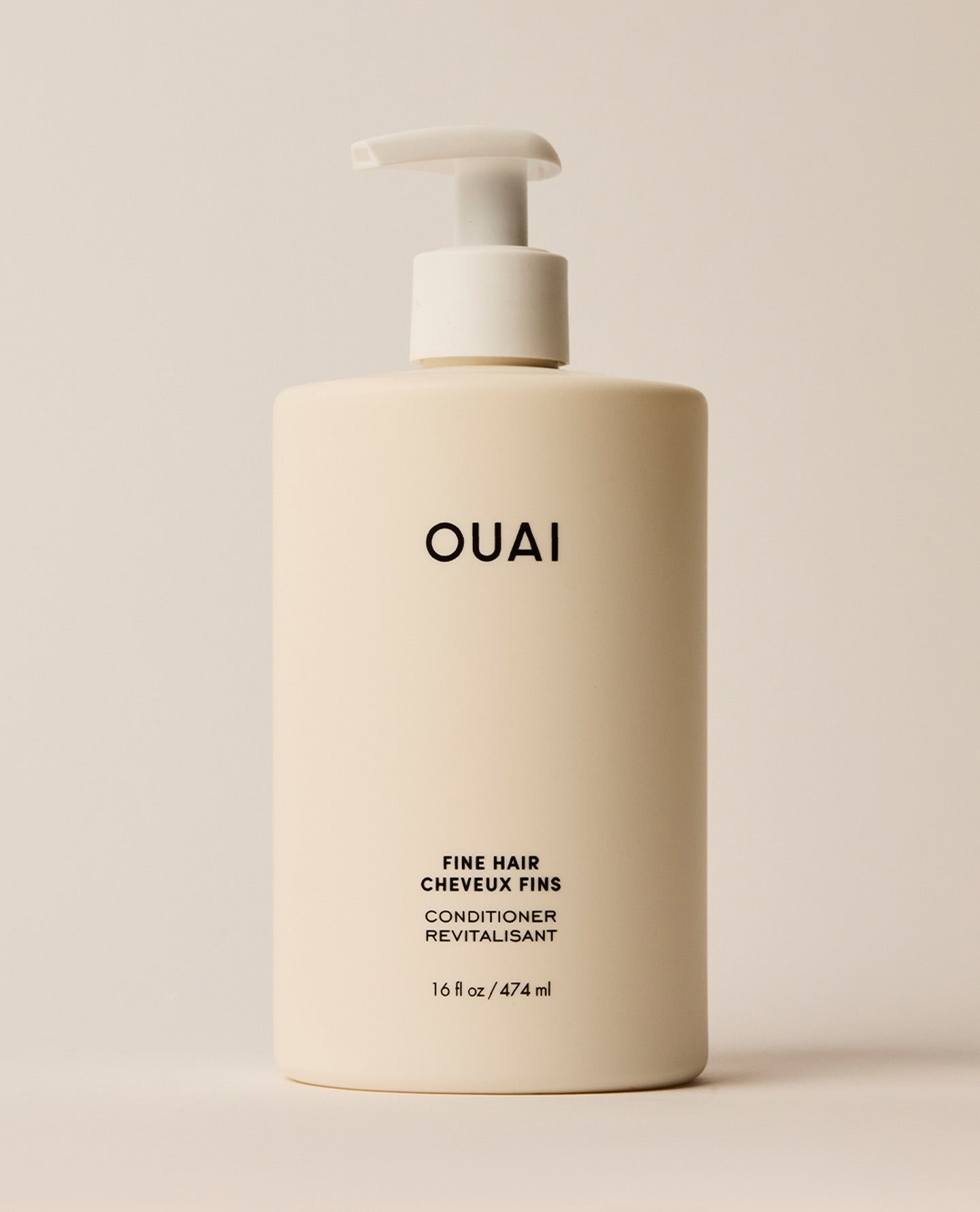 A large ivory OUAI Fine Hair Conditioner pump bottle stands upright against a softly lit cream background. Text: “OUAI”, “FINE HAIR”, “CHEVEUX FINS”, “CONDITIONER”, “REVITALISANT”, “16 fl oz / 474 ml”.