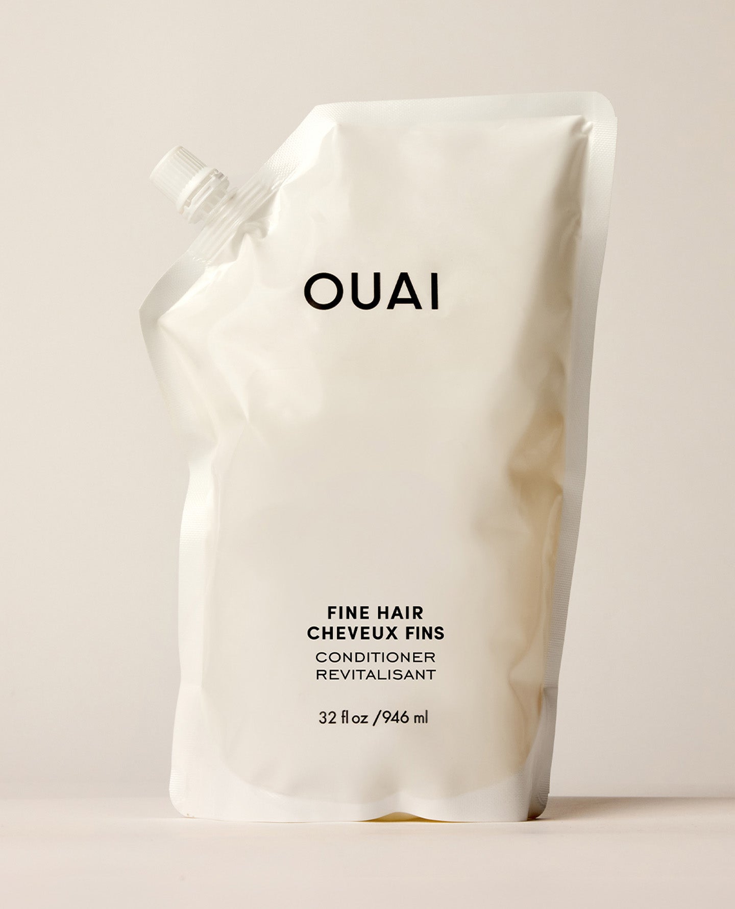 A white OUAI Fine Hair Shampoo refill pouch stands upright on a warm cream studio surface. Text: “OUAI”, “FINE HAIR”, “CHEVEUX FINS”, “SHAMPOO”, “SHAMPOOING”, “32 fl oz / 946 ml”.
