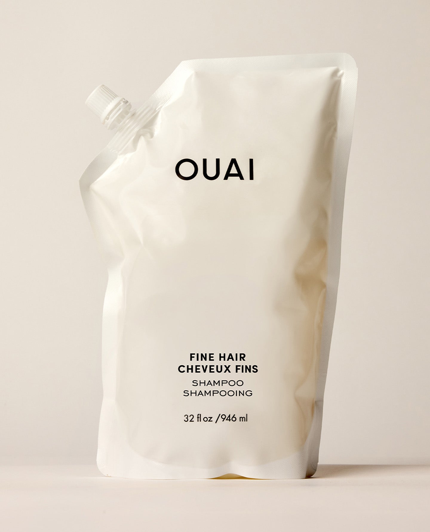 A white OUAI Fine Hair Conditioner refill pouch stands upright on a warm cream studio surface. Text: “OUAI”, “FINE HAIR”, “CHEVEUX FINS”, “CONDITIONER”, “REVITALISANT”, “32 fl oz / 946 ml”.