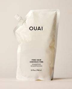 A white OUAI Fine Hair Conditioner refill pouch stands upright on a warm cream studio surface. Text: “OUAI”, “FINE HAIR”, “CHEVEUX FINS”, “CONDITIONER”, “REVITALISANT”, “32 fl oz / 946 ml”.