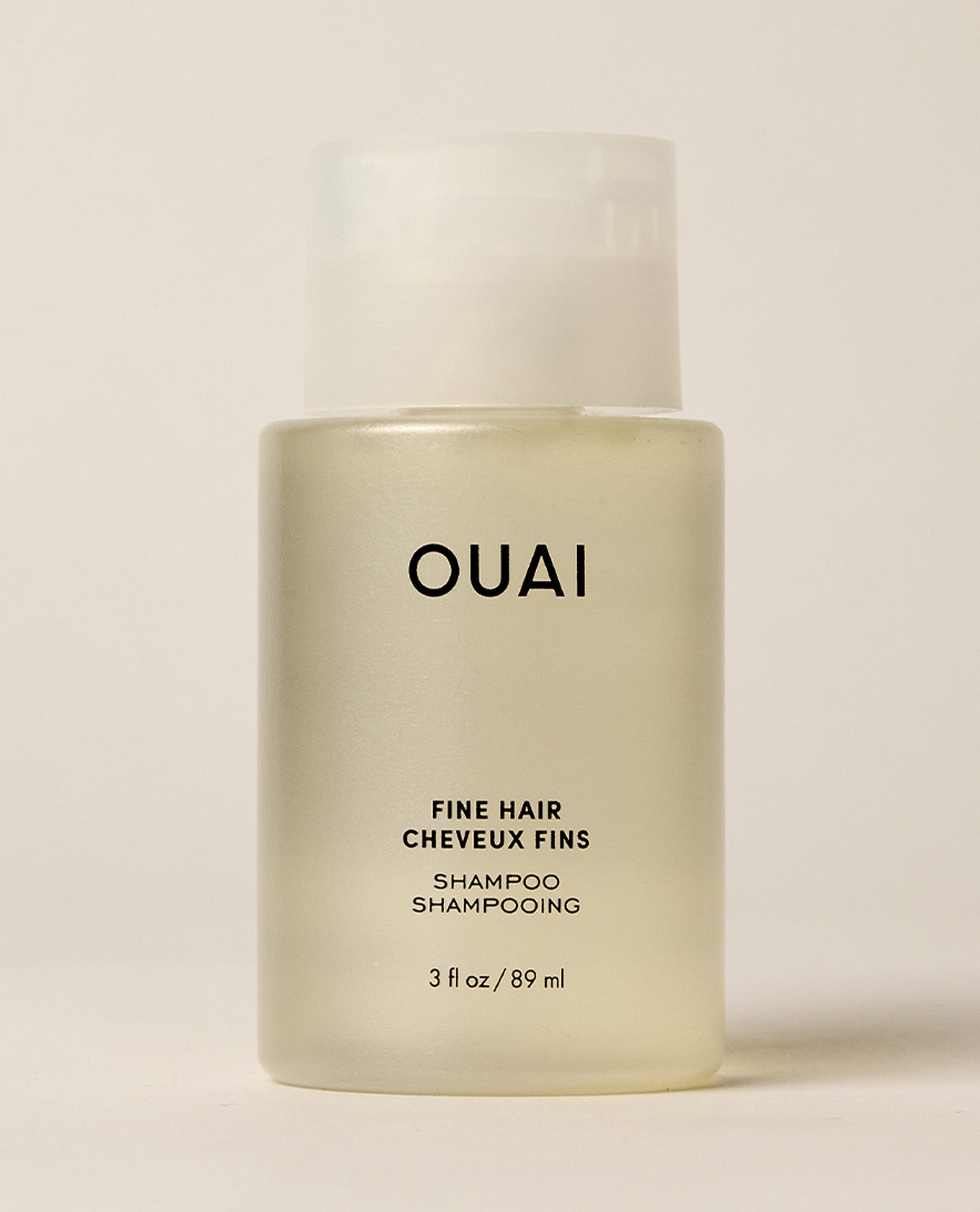A travel-sized translucent OUAI Fine Hair Shampoo bottle stands upright against a cream studio background. Text: “OUAI”, “FINE HAIR”, “CHEVEUX FINS”, “SHAMPOO”, “SHAMPOOING”, “3 fl oz / 89 ml”.