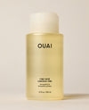 A translucent OUAI Fine Hair Shampoo bottle containing pale yellow liquid stands upright on a warm cream surface. Text: “OUAI”, “FINE HAIR”, “CHEVEUX FINS”, “SHAMPOO”, “SHAMPOOING”, “10 fl oz / 300 ml”.