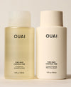 Two OUAI Fine Hair shampoo and conditioner bottles stand side by side on a cream studio surface, comprising a translucent yellow shampoo bottle and opaque ivory conditioner bottle.