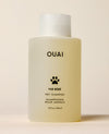 A translucent OUAI Fur Bébé Pet Shampoo bottle containing pale yellow liquid stands against a cream studio background. Text: “OUAI”, “FUR BÉBÉ”, “PET SHAMPOO”, “SHAMPOOING POUR ANIMAUX”, “16 fl oz / 474 ml”.