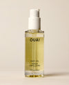 A clear OUAI Hair Oil pump bottle containing pale yellow liquid stands against a softly lit cream background. Text: “OUAI”, “HAIR OIL”, “HUILE CAPILLAIRE”, “1.5 fl oz / 45 ml”.