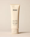 An ivory OUAI hand cream tube stands upright on a warm cream studio surface. Text: “OUAI”, “HAND CRÈME”, “CRÈME MAINS”, “RUE ST. HONORÉ”, “3 fl oz / 88.7 ml”.