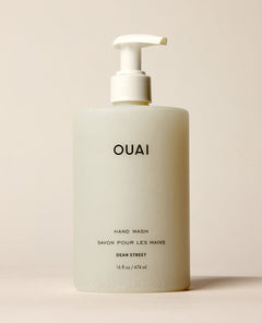 A frosted OUAI Dean Street Hand Wash pump bottle stands upright against a warm neutral background. Text: “OUAI”, “HAND WASH”, “SAVON POUR LES MAINS”, “DEAN STREET”, “16 fl oz / 474 ml”.