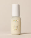 A larger frosted OUAI St. Barts Leave-In Conditioner travel bottle stands upright against a softly lit cream background, finished with iridescent branding and a rounded white cap.