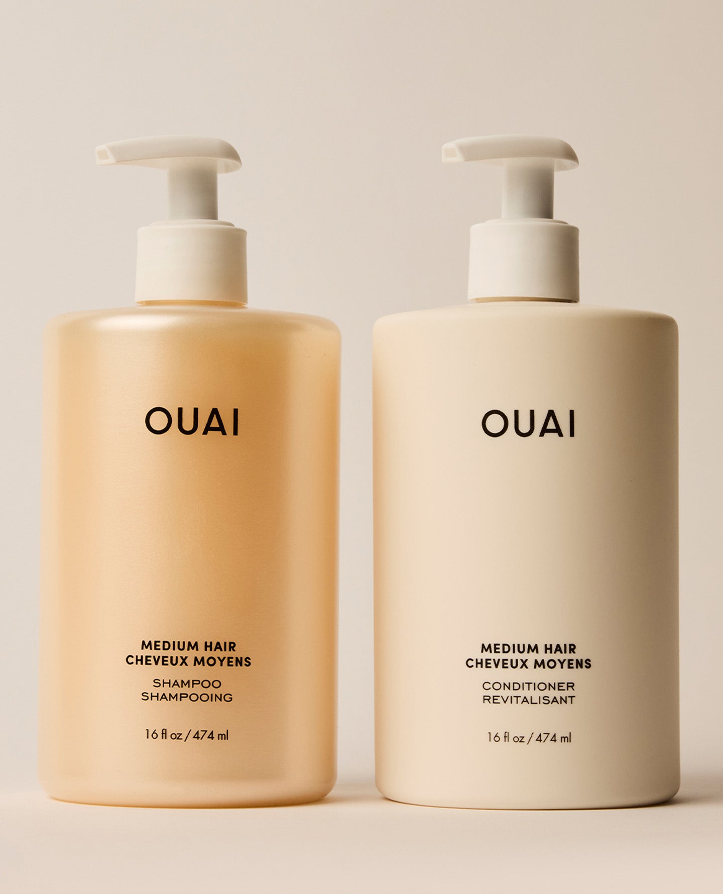 Two jumbo OUAI Medium Hair shampoo and conditioner pump bottles stand side by side, with amber-toned shampoo and cream conditioner packaging against a neutral studio background.