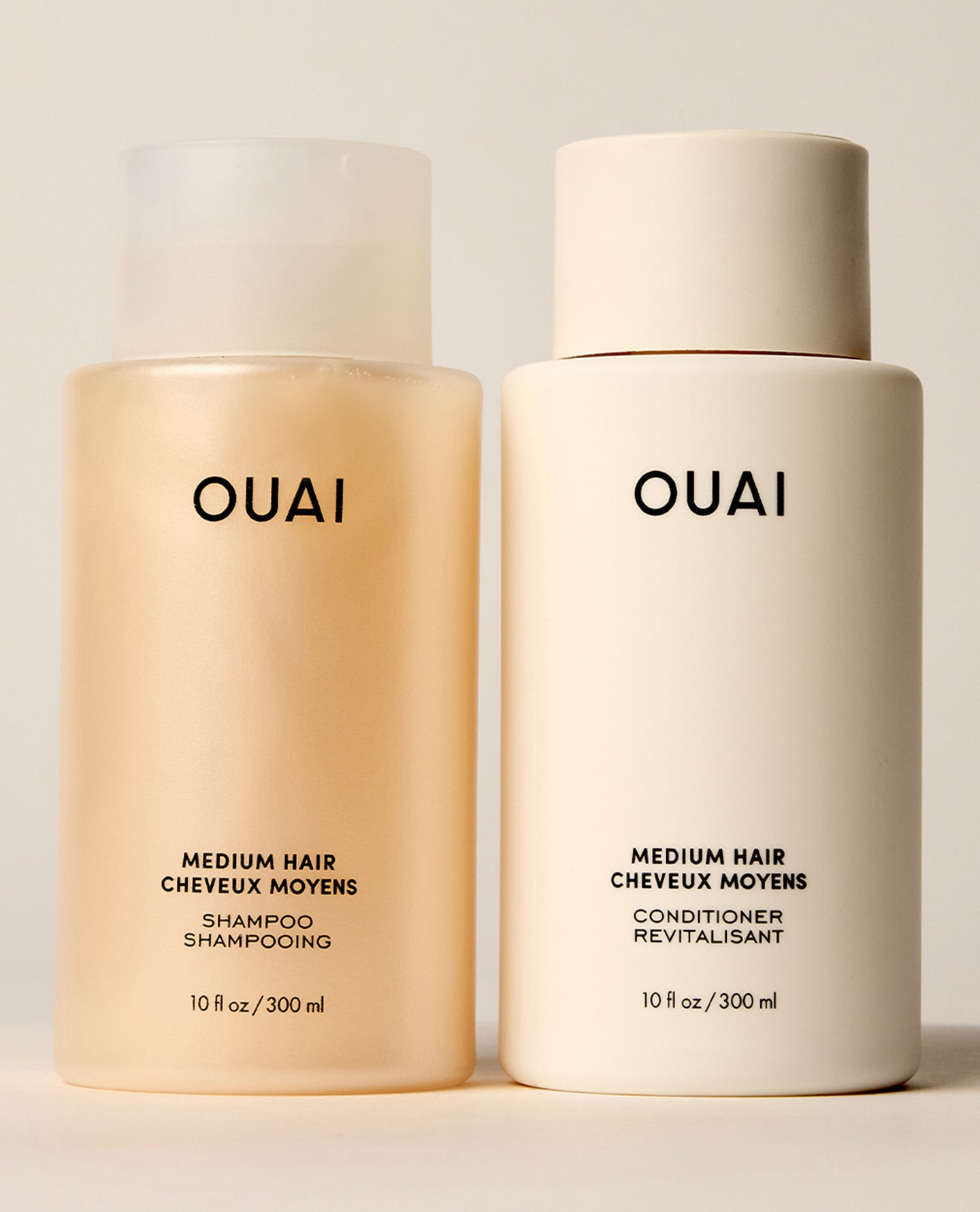 Two standard-size OUAI Medium Hair shampoo and conditioner bottles stand side by side, featuring translucent amber shampoo and opaque cream conditioner packaging.