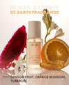 A bottle of OUAI fragrance centered on a clean white background, surrounded by a sliced dragon fruit, orange blossom stem, and orange slice. Text at the top reads 'BEACHY & CITRISY ST.